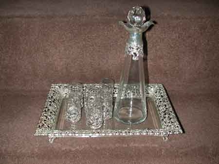 A Victorian composed liquer set somprising of a spreading cylindrical decanter with prismatic stopper, six glasses, a rectangular tray, the mounts and the border pierced and embossed with cherubic masks, fanciful birds and foliate scrolls the tray with a bevelled glass field, cartouche shaped scroll cast feet. Inscribed Sunshine Middlewood Polo Cup, 1900 Silver marked John and Wiliam Deaken Chester and Birmingham 1897